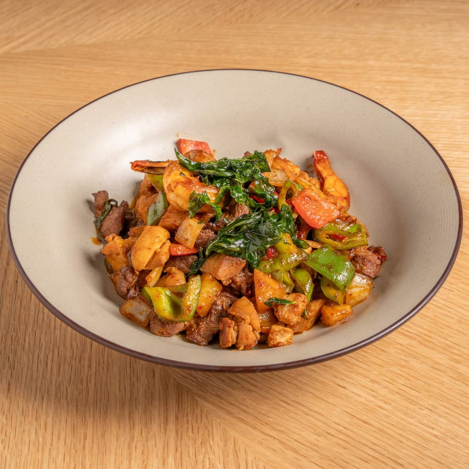 A Chinese dish with shrimp, beef, chicken, bell peppers, and basil in a light brown bowl.