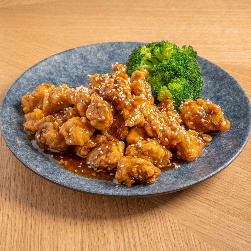 THAIKULA's Chinese orange chicken with sesame seeds and a side of broccoli on a gray plate.