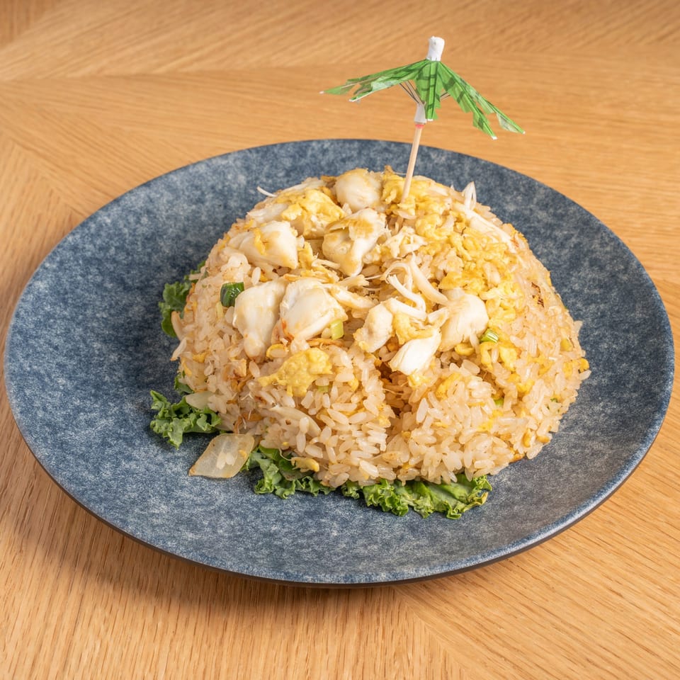 Crab fried rice with scrambled egg and a small green paper umbrella on a blue plate.