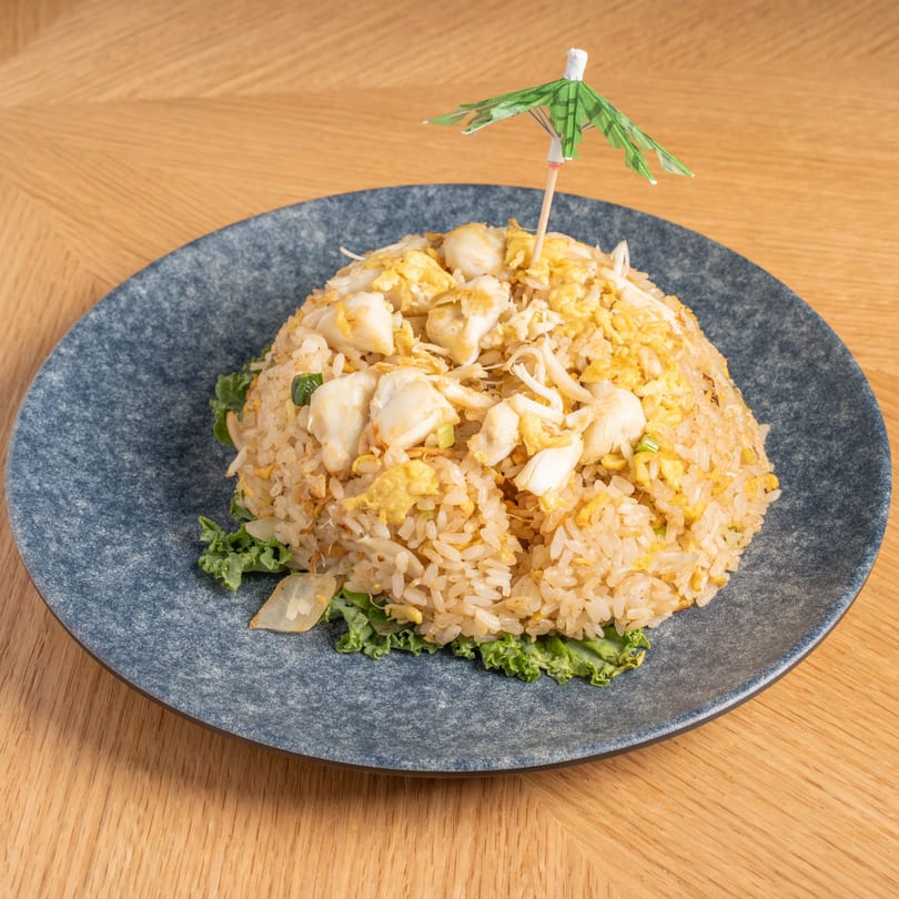 Crab fried rice with scrambled egg and a small green paper umbrella on a blue plate.