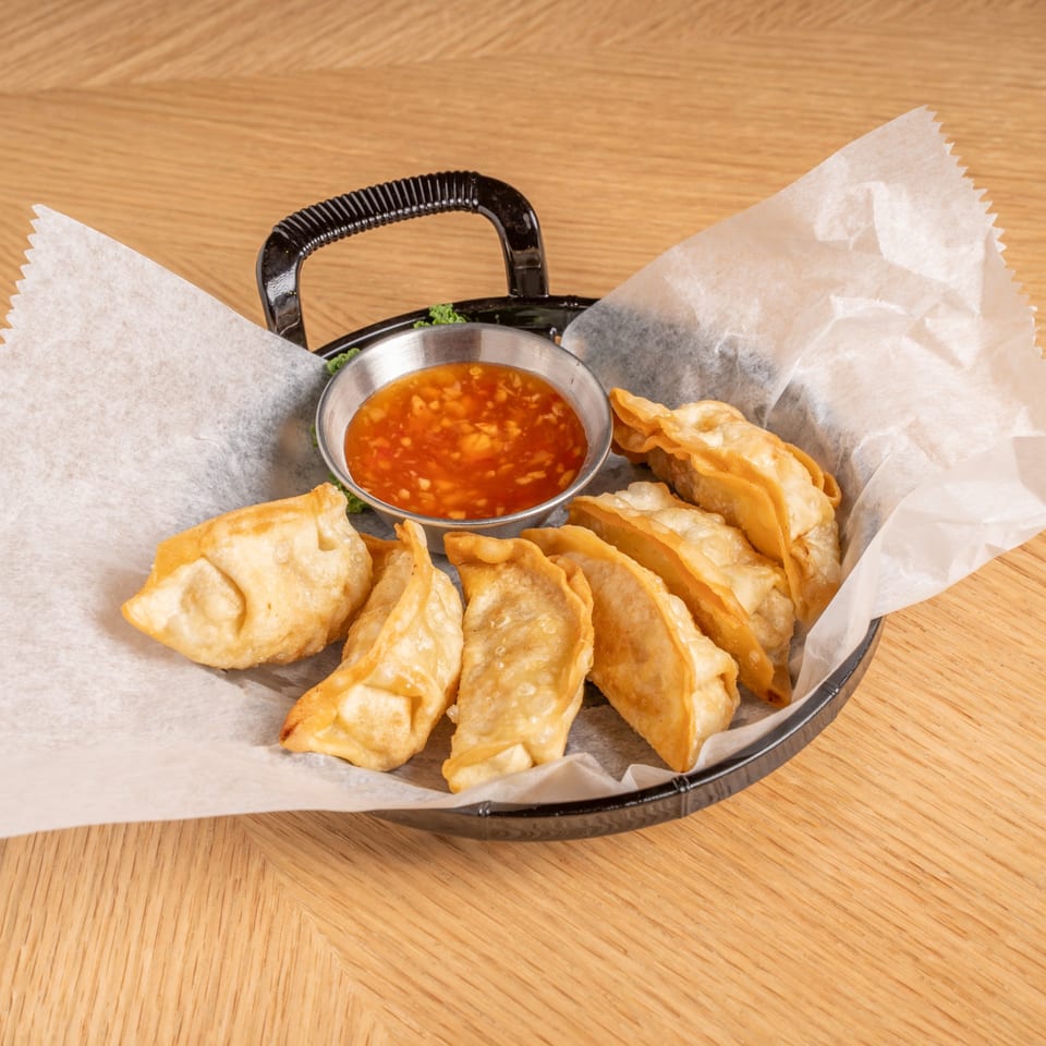A black basket of crispy fried Chinese dumplings with a side of sweet chili sauce.