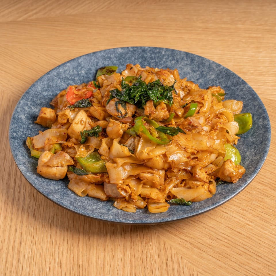 Chinese stir-fried noodles with chicken, green peppers, and basil on a blue plate.