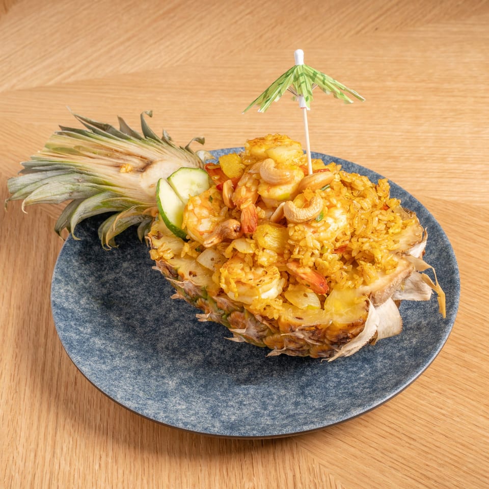 Pineapple fried rice with shrimp and cashews, served in a pineapple half with a cocktail umbrella.