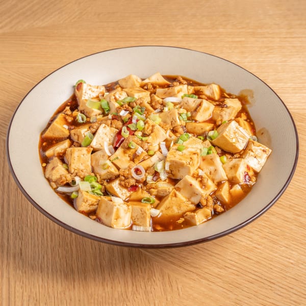 A bowl of Chinese Mapo Tofu with minced meat and green onions on a wooden table.