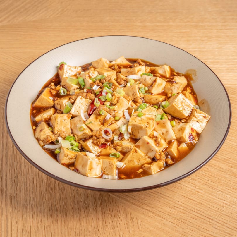 A bowl of Chinese Mapo Tofu with minced meat and green onions on a wooden table.