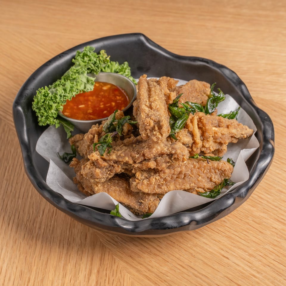 Crispy fried chicken wings with basil, kale, and sweet chili sauce in a black bowl.