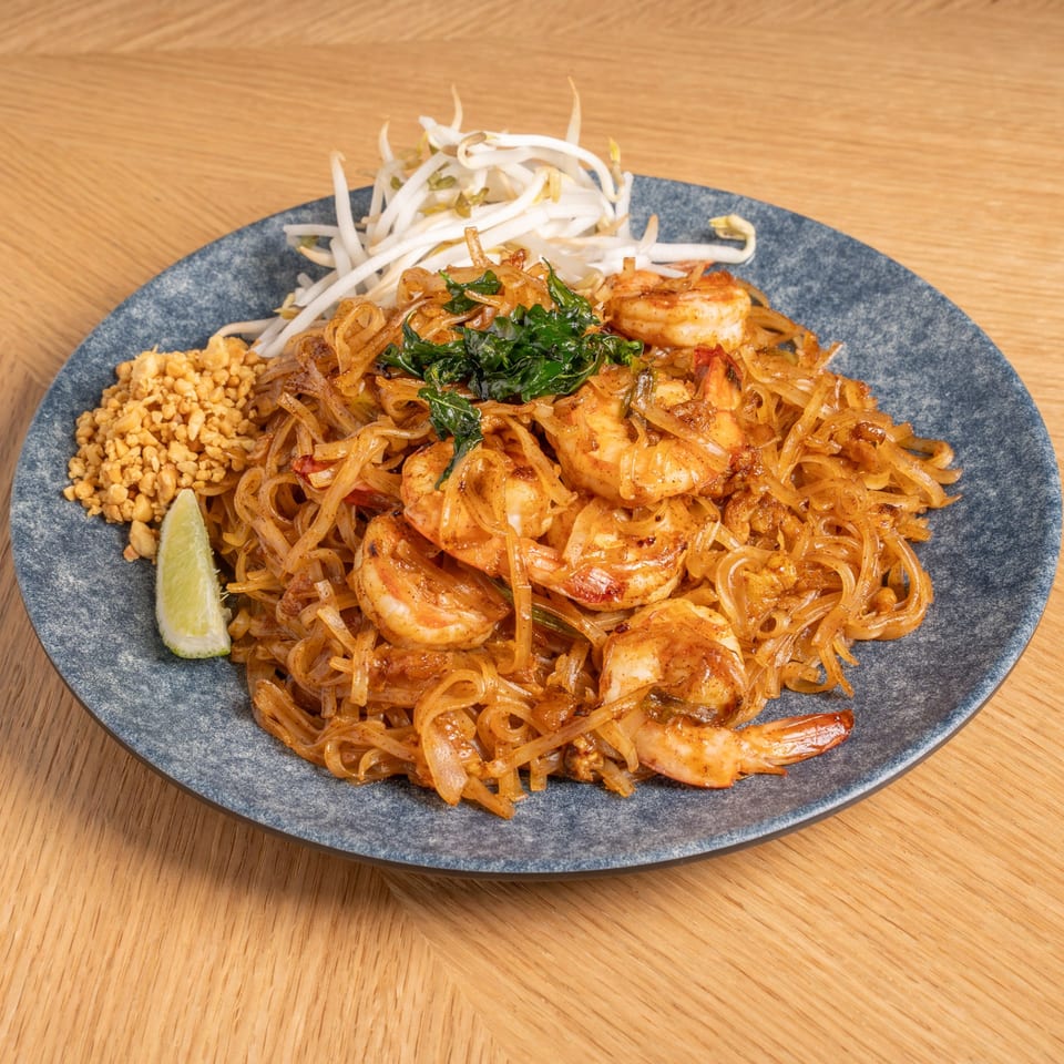 A plate of Pad Thai with shrimp, bean sprouts, crushed peanuts, and a lime wedge.