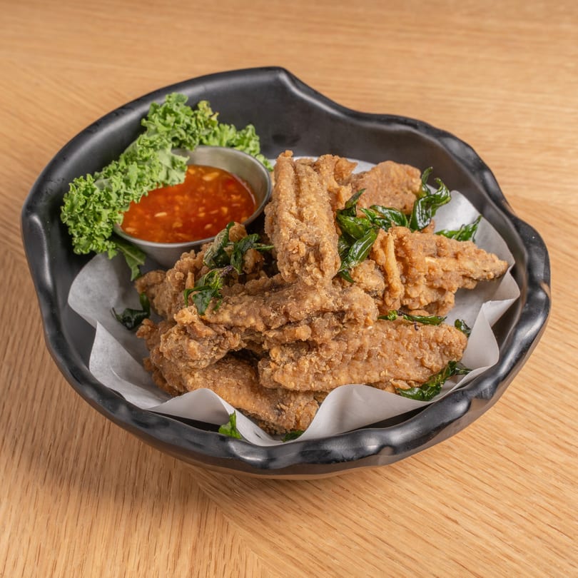 Crispy fried chicken pieces with basil, served with sweet chili sauce and lettuce in a black bowl.