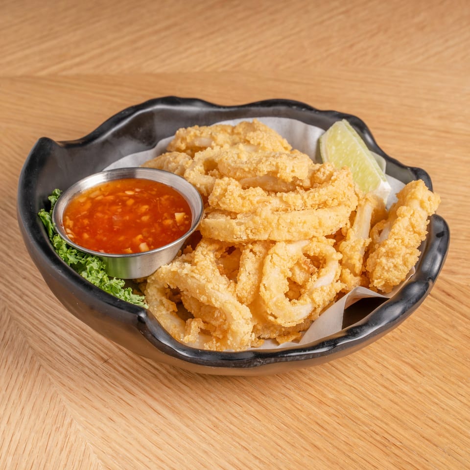 Crispy fried calamari rings with a side of sweet chili sauce and a lime wedge.